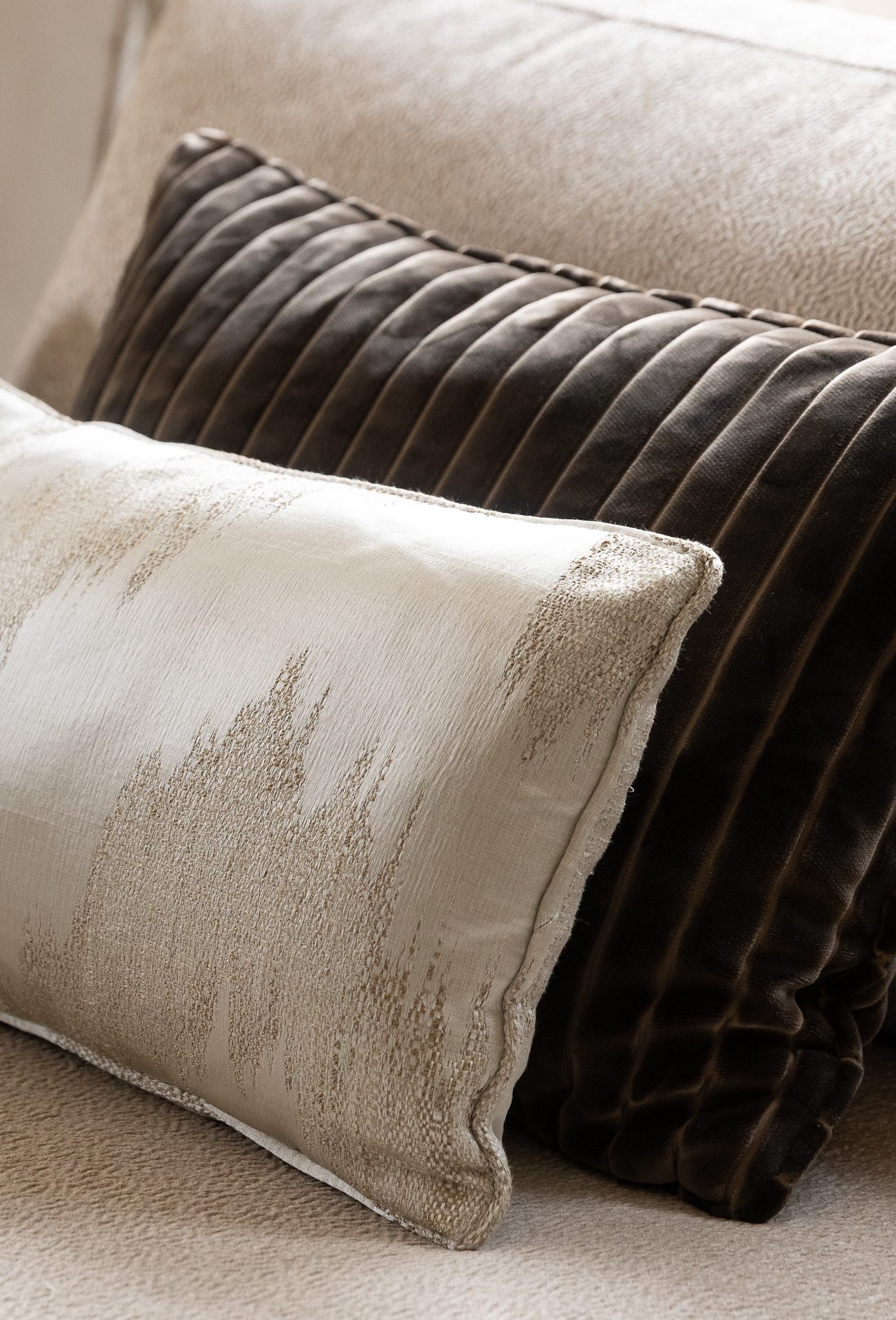 A small cream cushion with a silvered ikat pattern, resting against a larger dark brown ribbed-velvet cushion on a pale chair