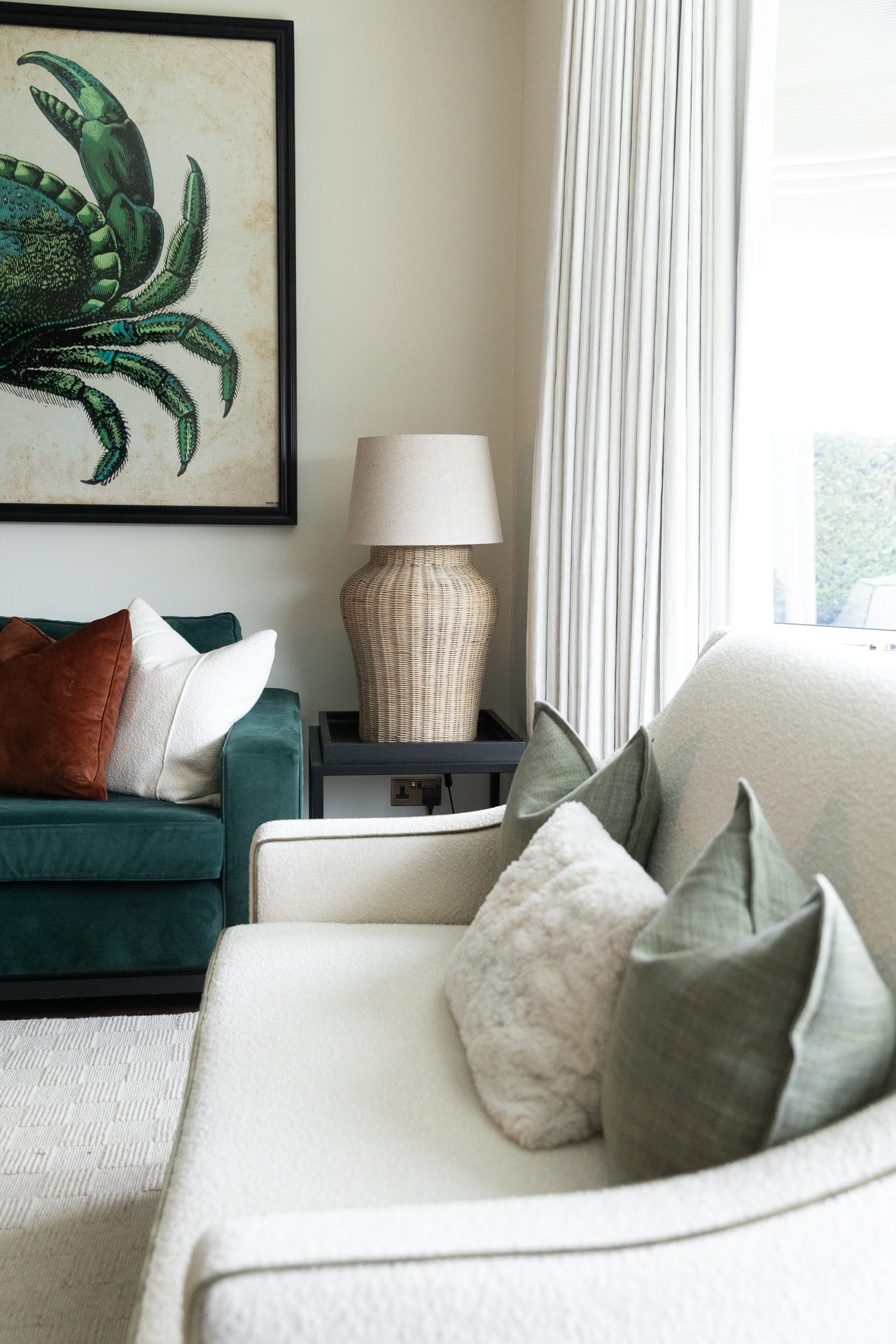 The cream armchair at Bamburgh with a rattan pendant and a glimpse of the bay window