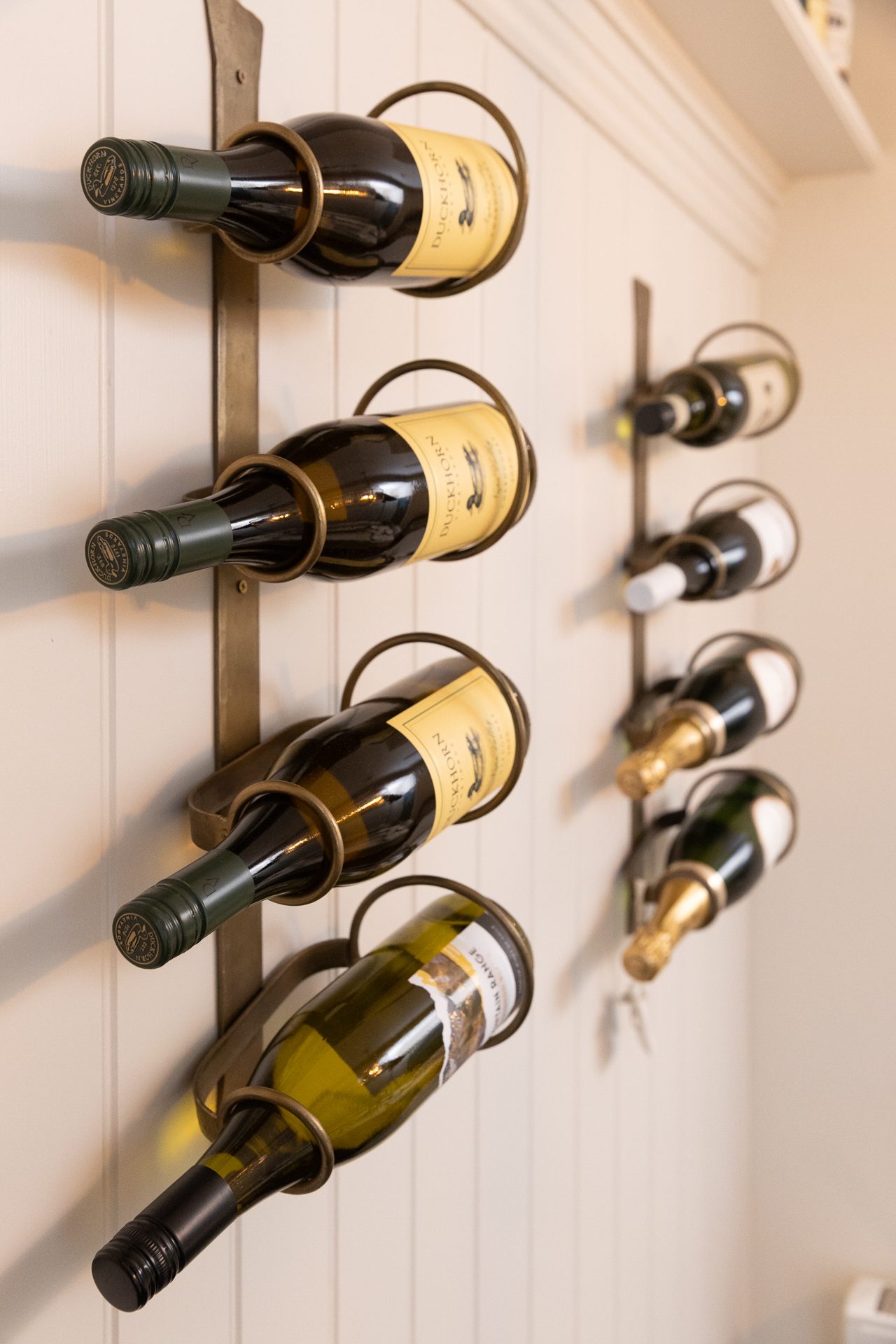 A framed wine rack on the panelled wall of the Bamburgh dining room, brass hoops holding bottles in a ladder