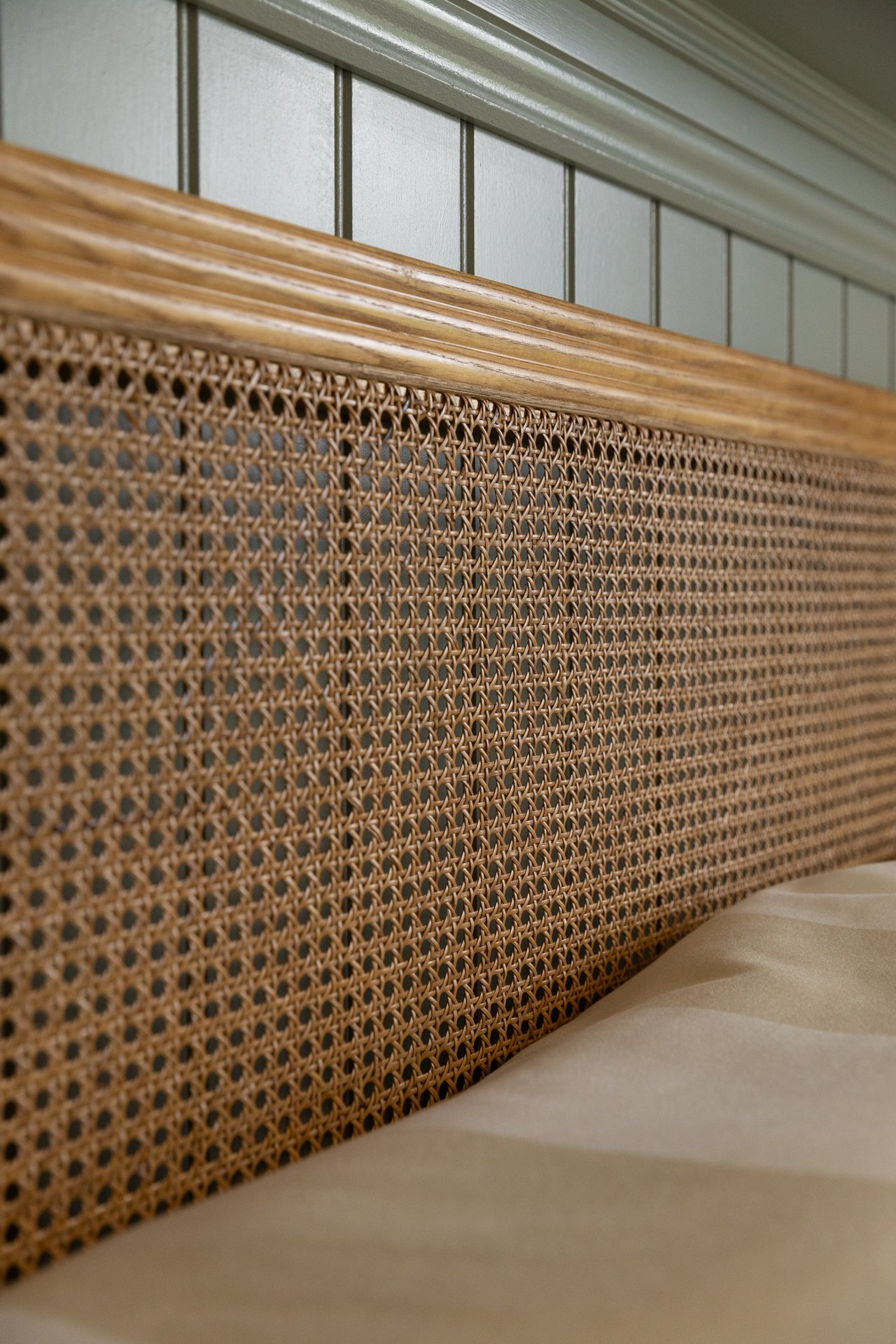 Close detail of the rattan-cane headboard against sage panelling