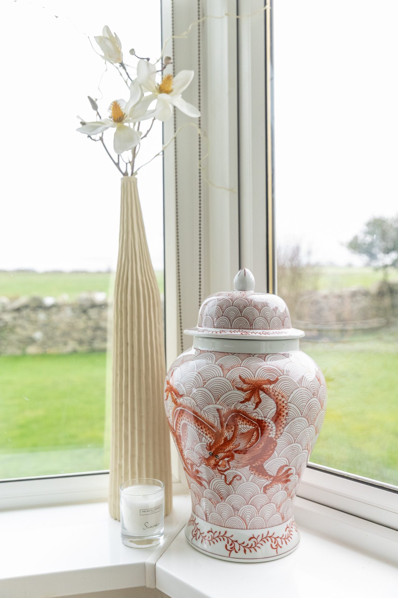 A ginger jar with a painted dragon sitting in the Bamburgh living room window, drystone wall and sea beyond