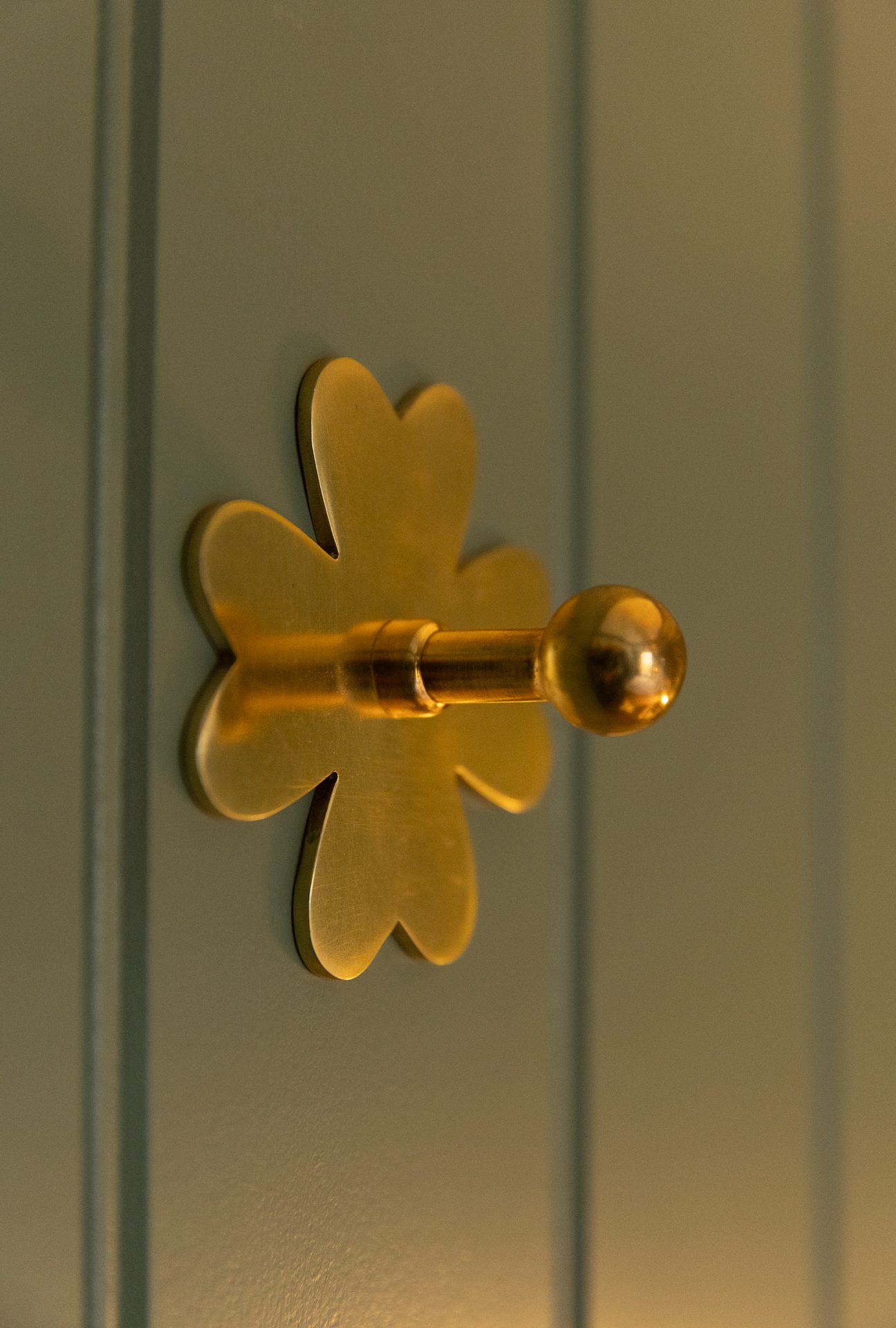 A brass flower-shaped cabinet pull set into the sage panelling of the Bamburgh master bedroom