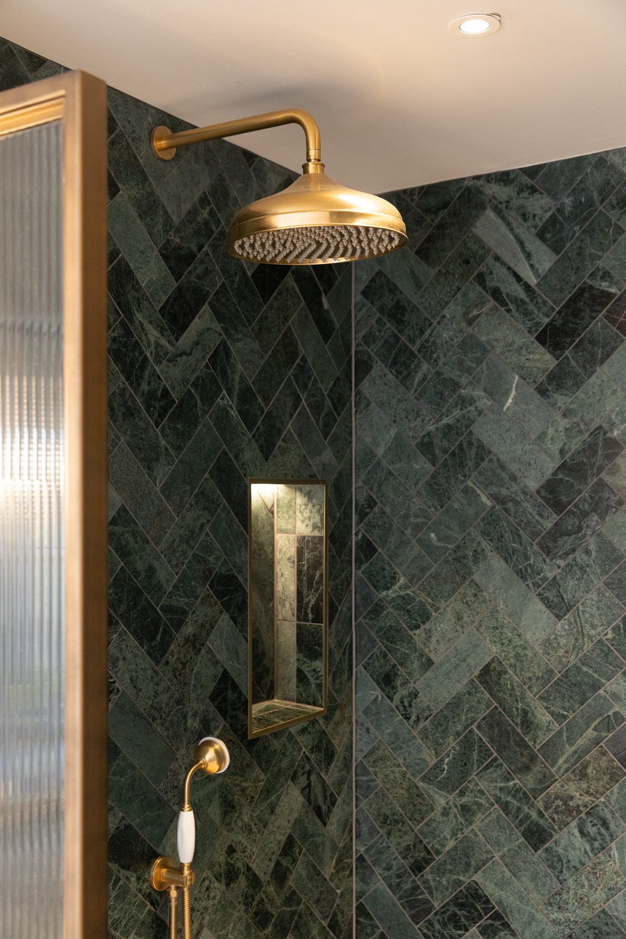 Green marble laid in herringbone inside the en-suite shower, brass showerhead and a single lit niche