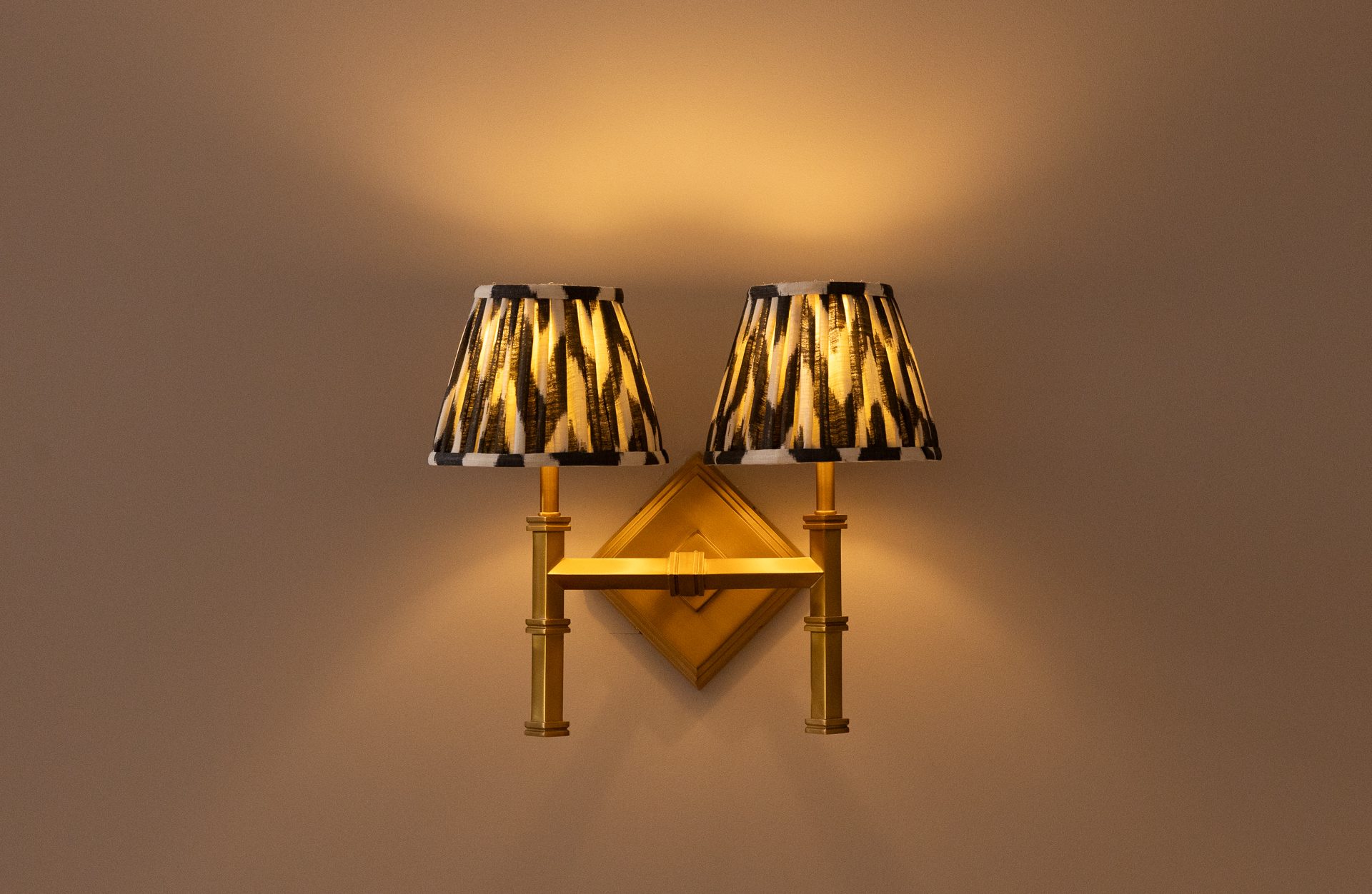 Twin brass wall sconces with ikat-stripe shades, casting warm light