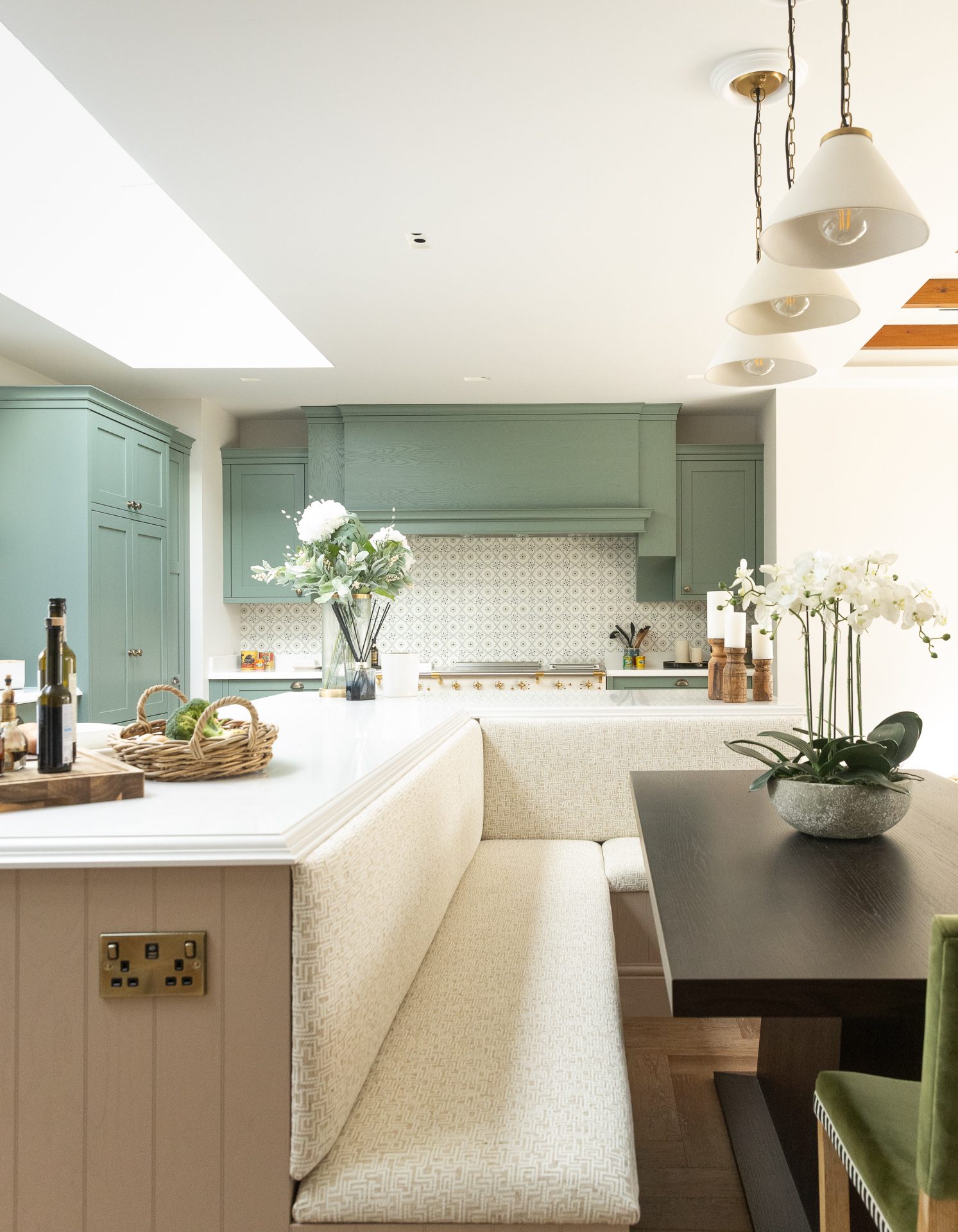 The sage green kitchen with built-in banquette seating, island, and pendant lights