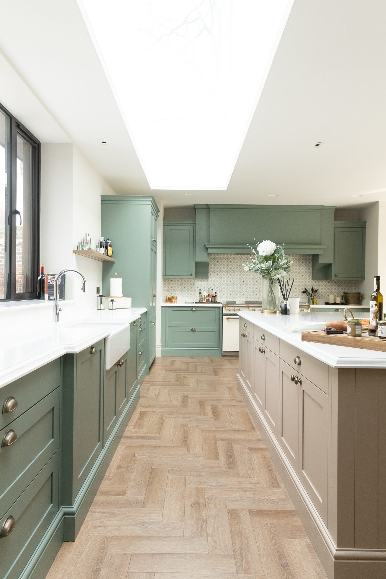The kitchen galley view, sage green units and herringbone flooring running towards the Lacanche range under a wall of skylights
