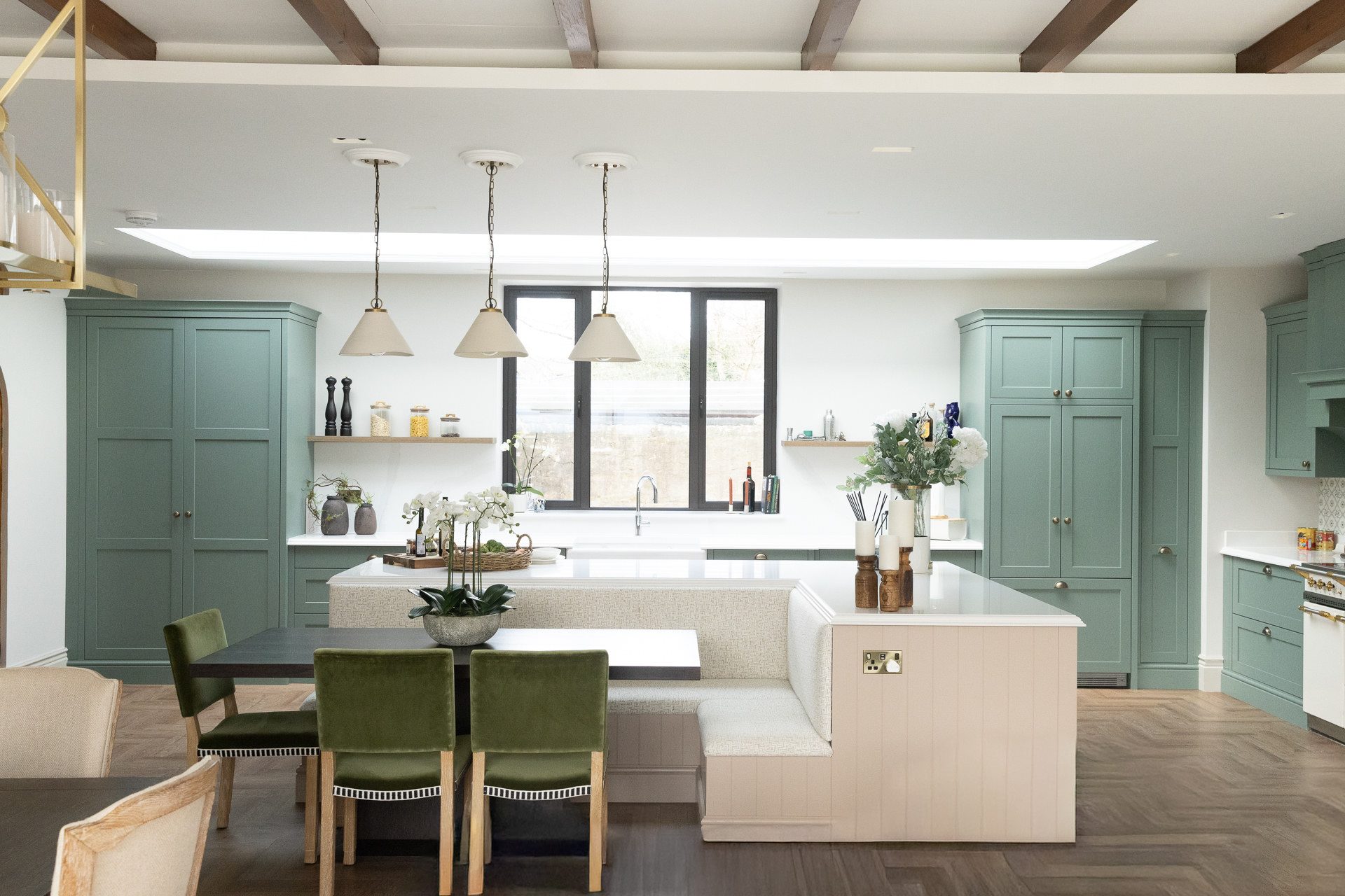 Sage green kitchen with triple pendants over the island and a built-in banquette at the far end, herringbone parquet flooring