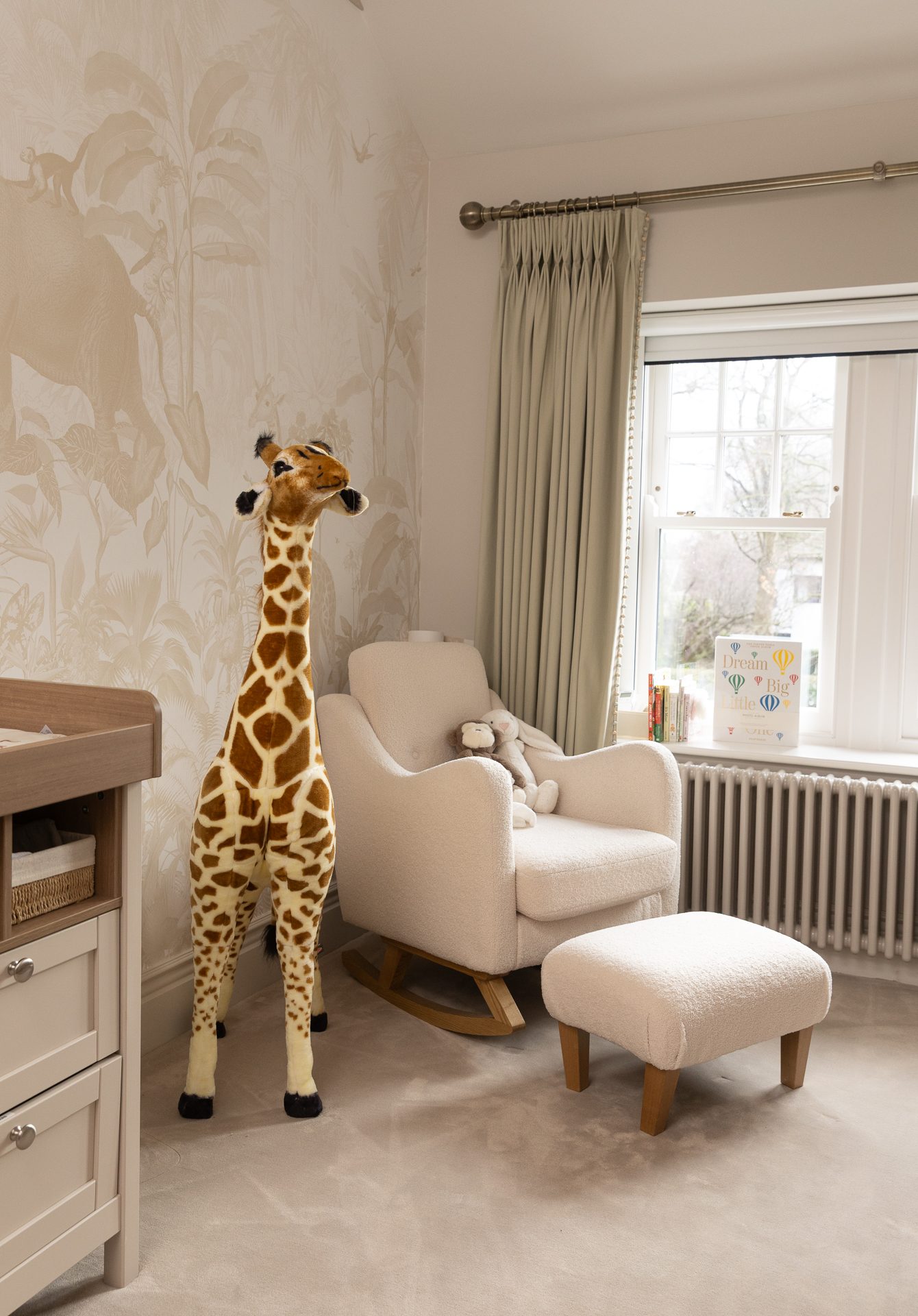 The nursery with botanical wallpaper, boucle rocking chair, and a standing giraffe by the window