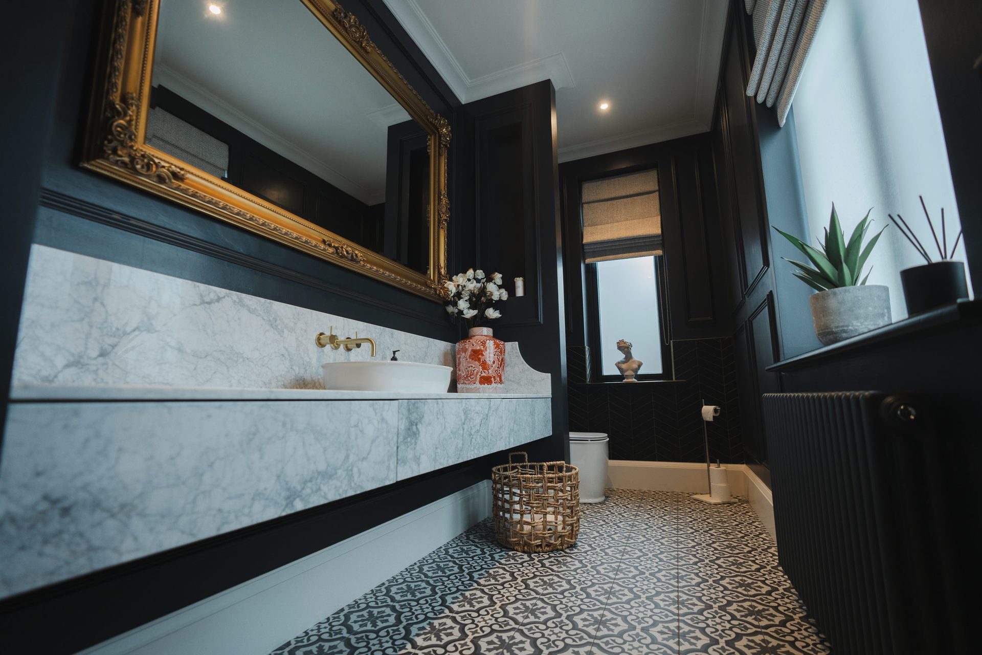 The W.C held straight-on, ornate gilded mirror above a floating marble vanity with chrome taps and a patterned ginger jar on the counter