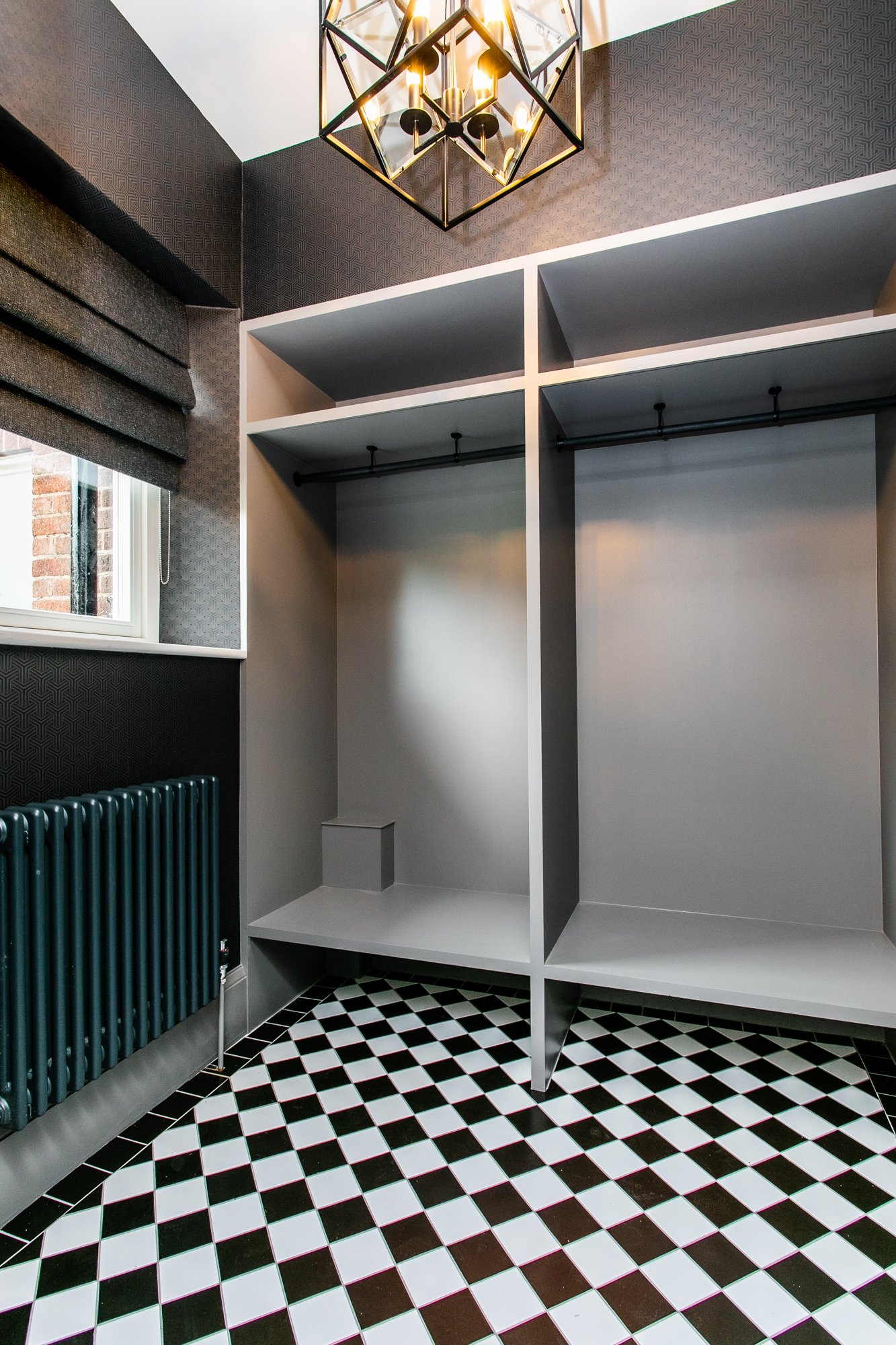 A cloak and storage run with open joinery, a geometric black iron pendant, black and white checkerboard tile underfoot