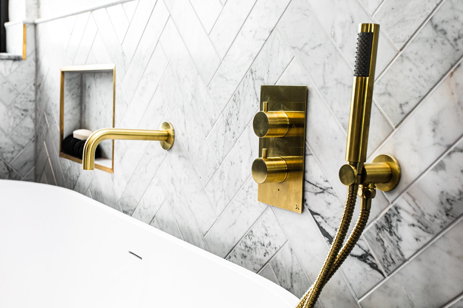 A brass thermostatic shower valve and hand-shower cradle, fixed to a marble wall