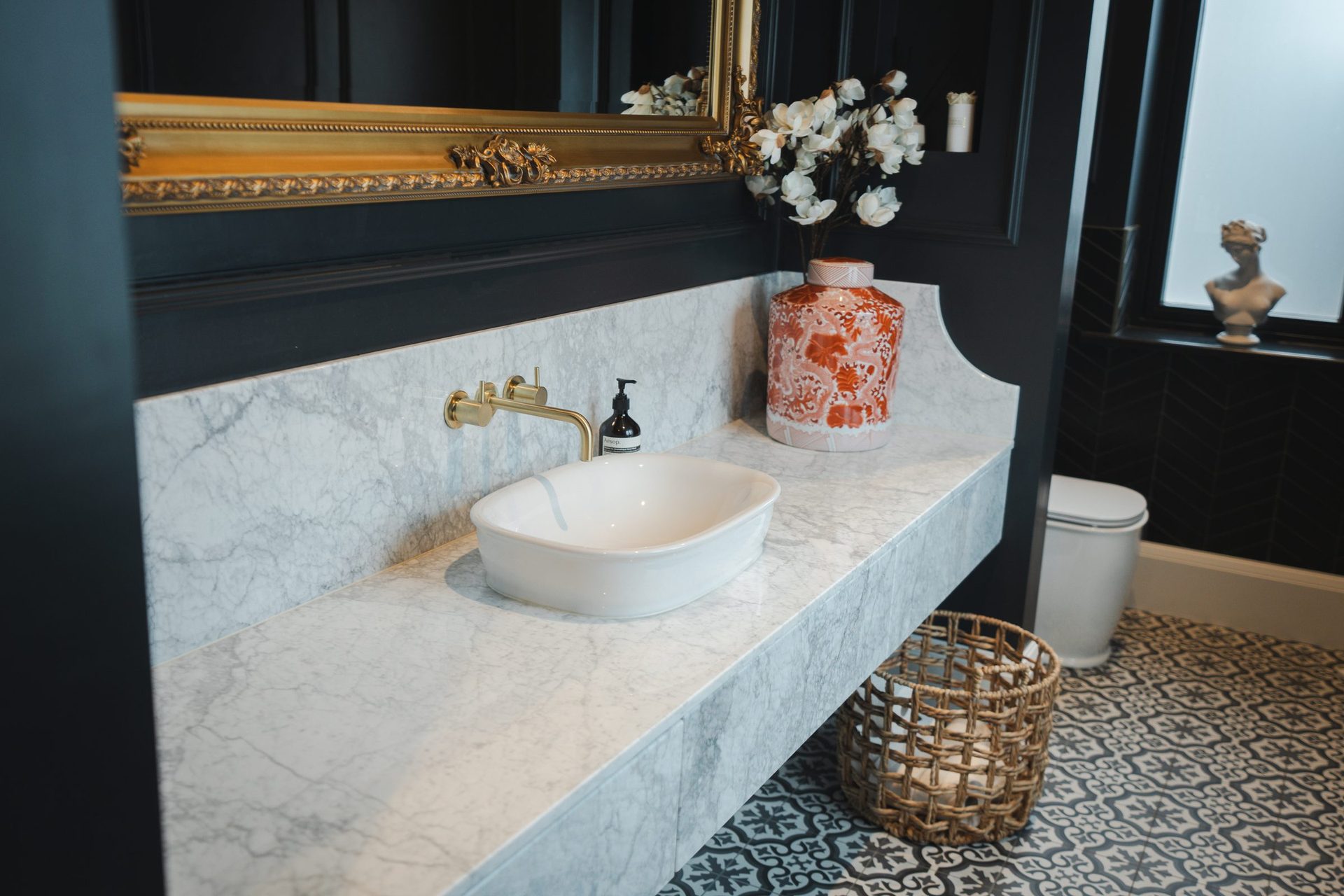A patterned ginger jar on the marble vanity in the W.C, next to a woven basket holding folded towels