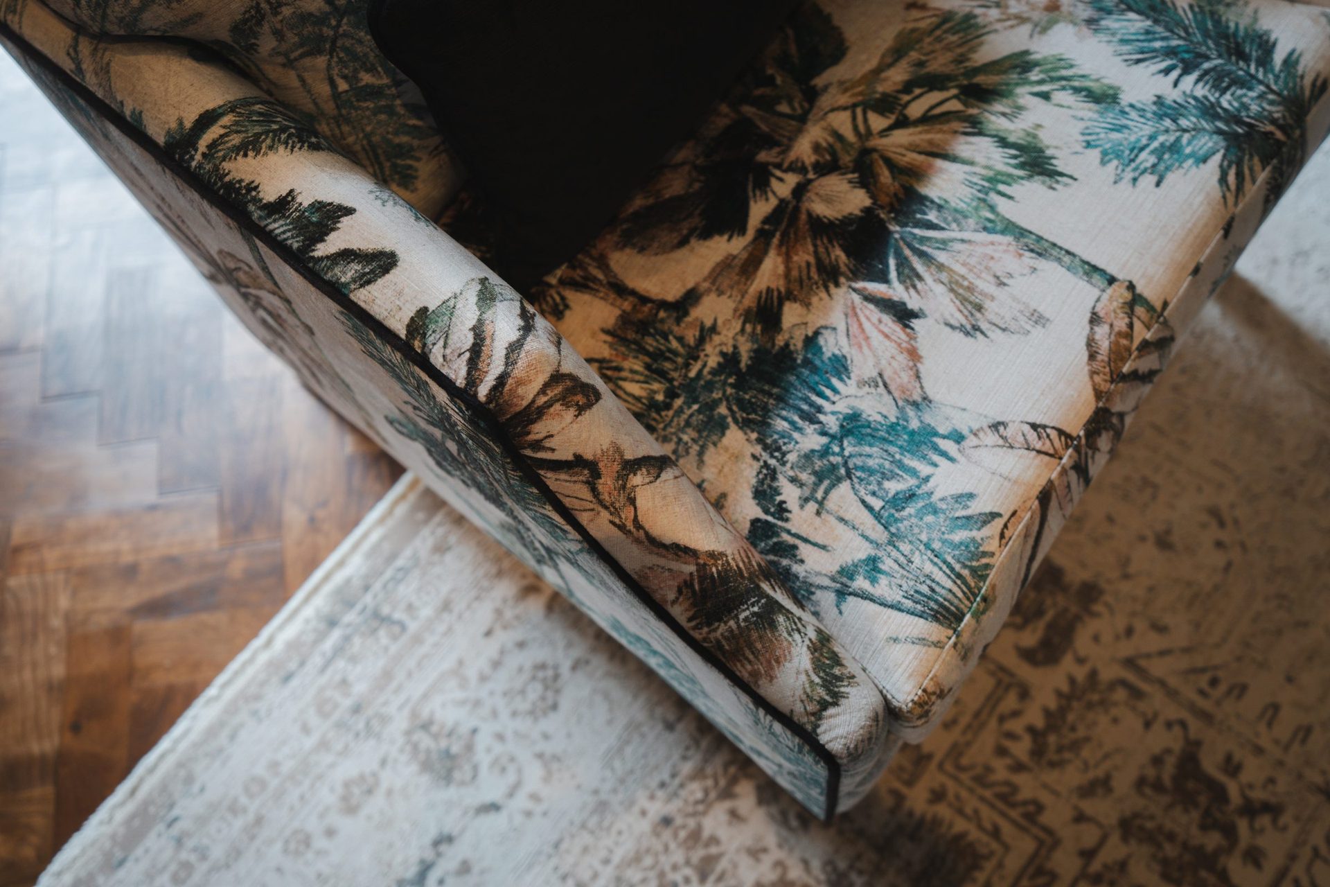 Detail of a palm-print occasional chair corner, folded against a parquet floor