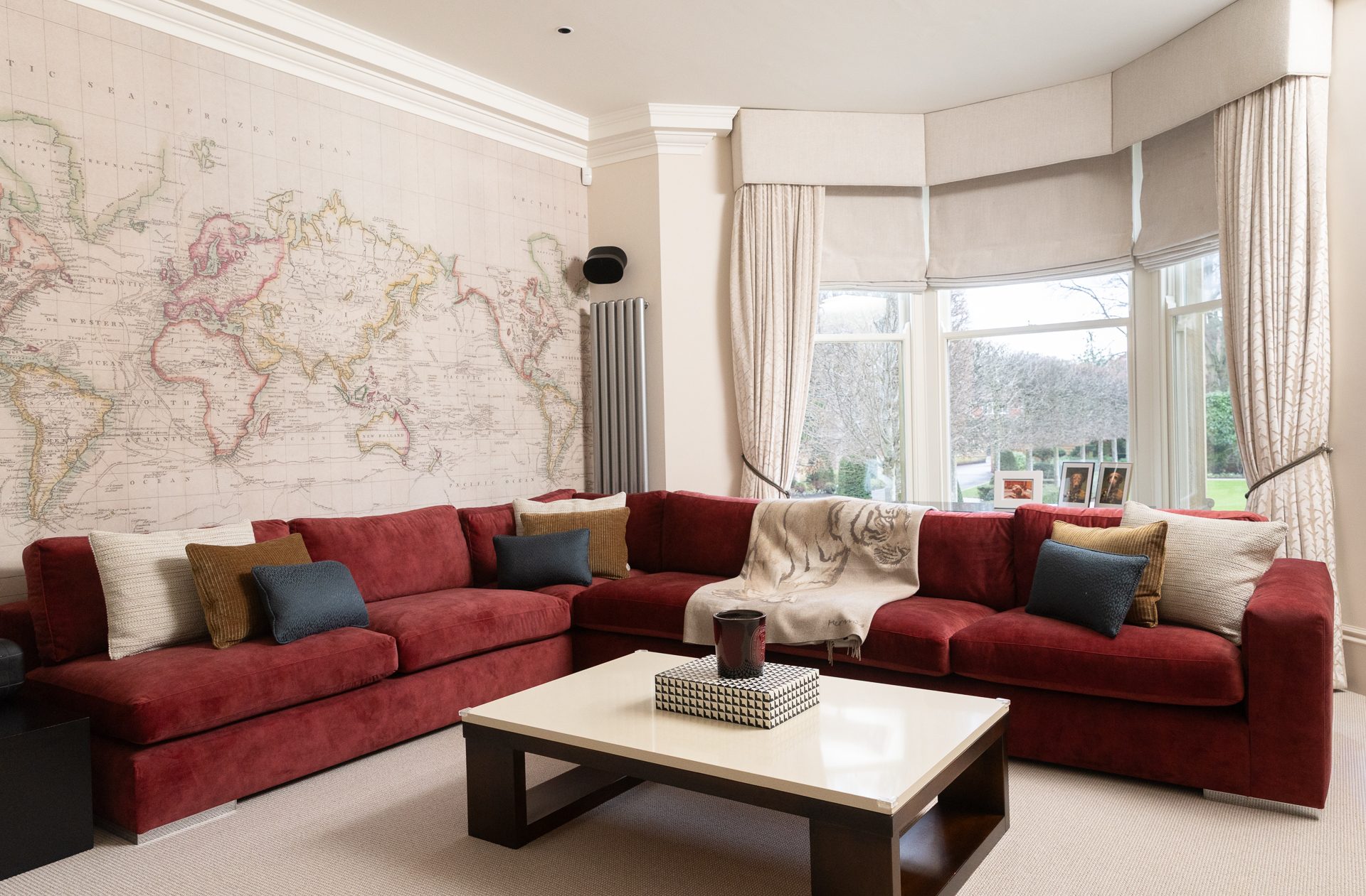 The Springfield lounge, a red velvet sectional set against vintage map wallpaper with a coffee table and the bay window beyond