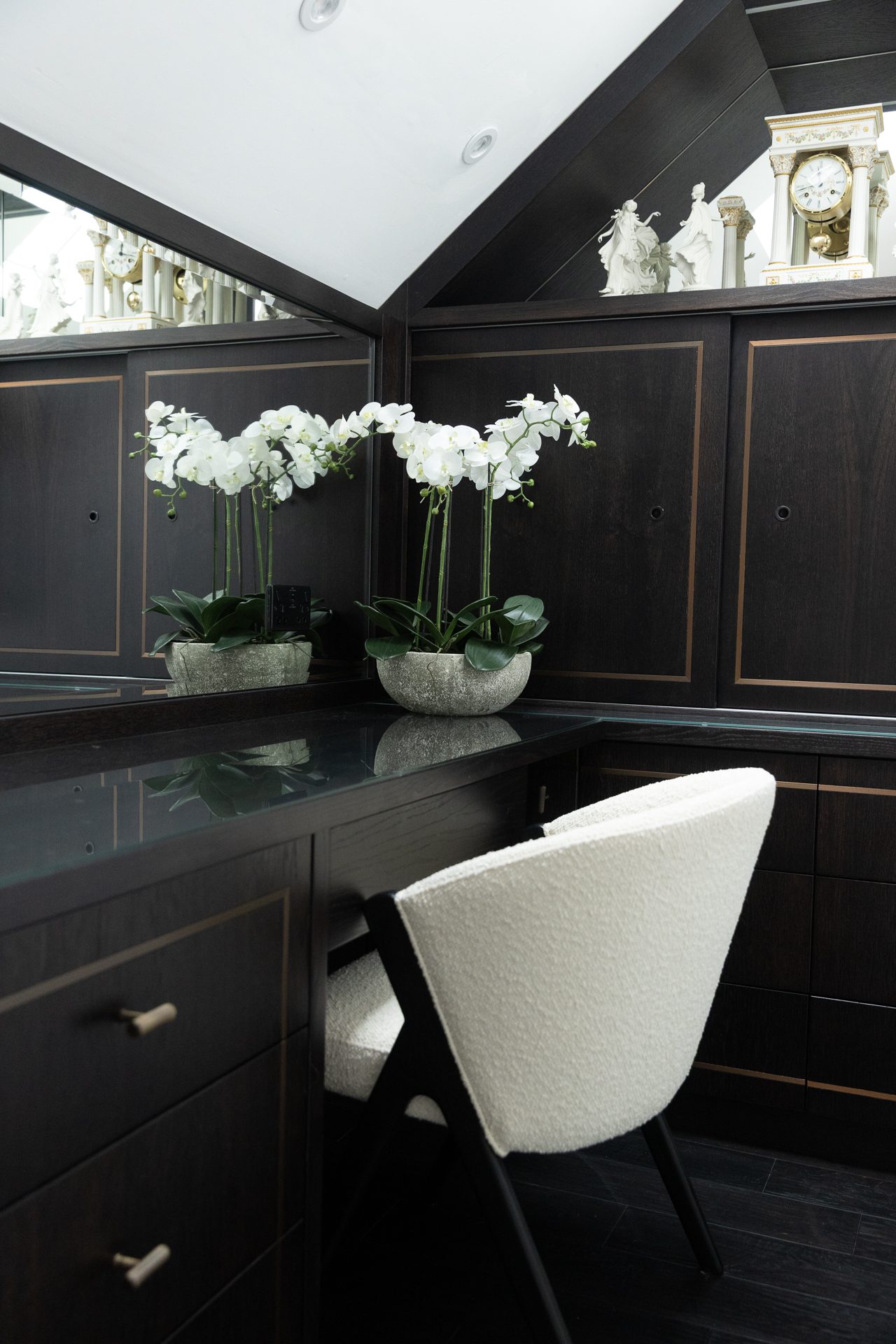 Orchids against dark brass-lined cabinetry and a white boucle chair pulled to the dressing counter