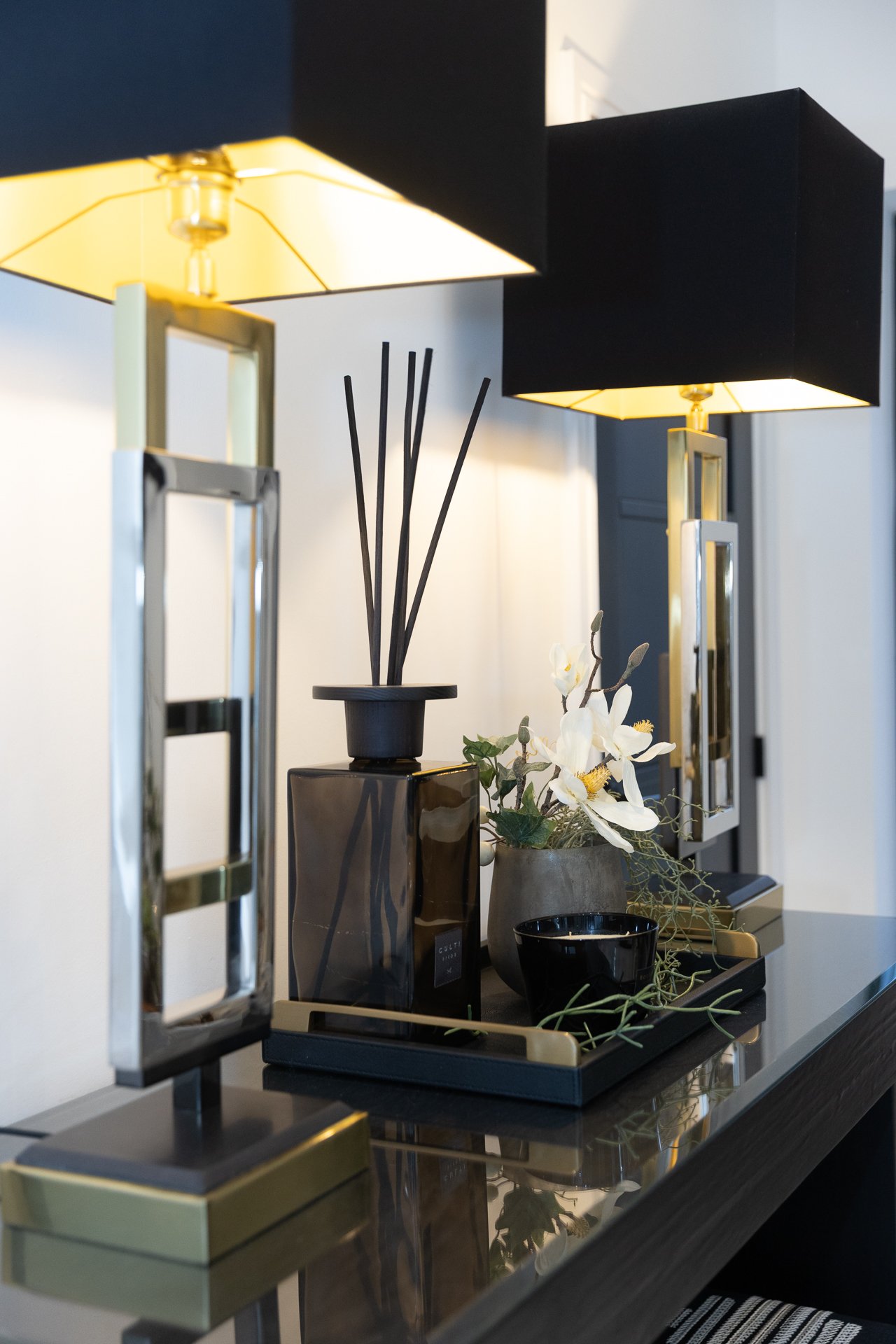 A pair of lantern-style table lamps with brass bases and black linen shades, lit against the dark console