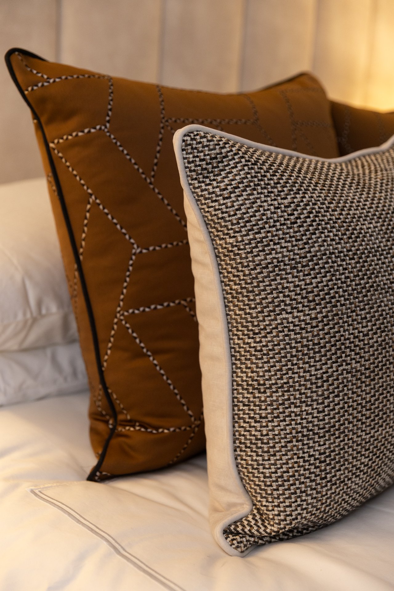 Close detail of tweed and rust cushions stacked against the pillows