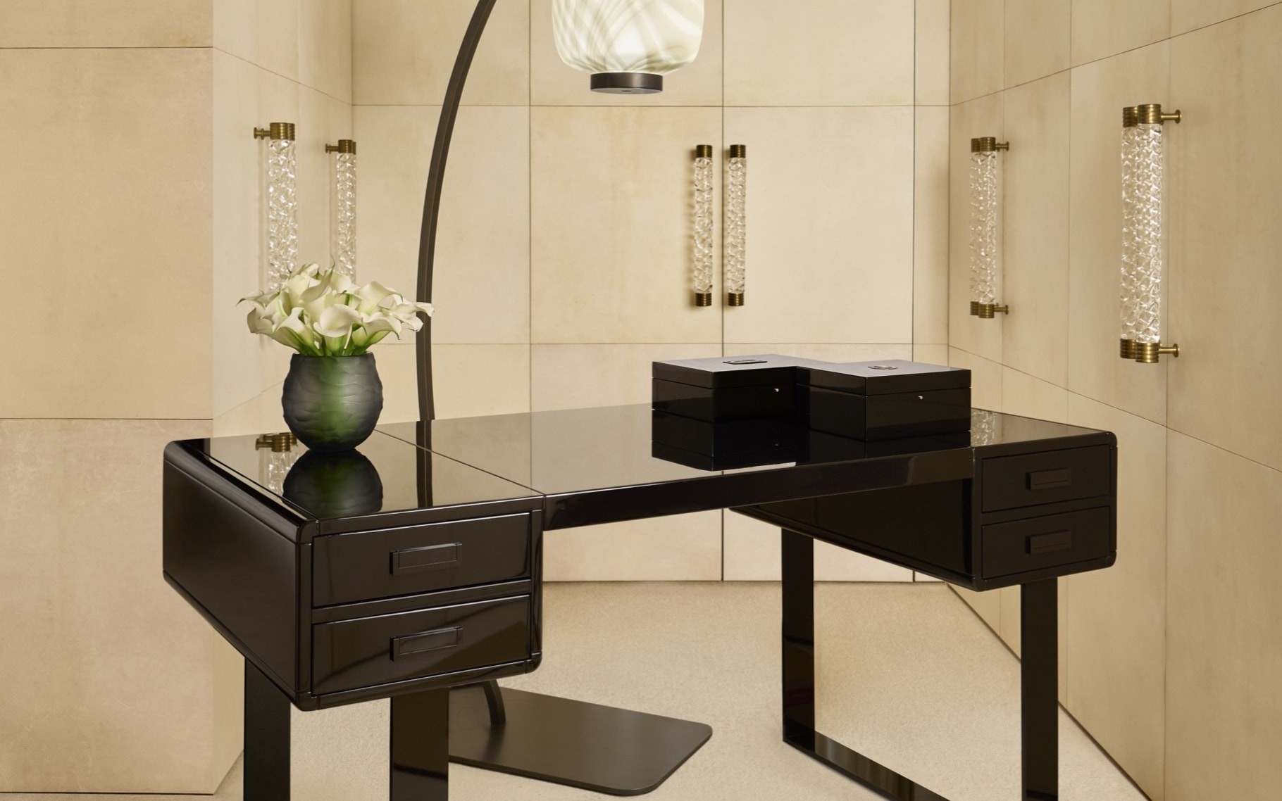 An Armani Casa black lacquered desk with brass-and-glass wall sconces, an arched marbled-glass floor lamp and calla lilies in a dark vase, set in a cream leather panelled dressing room — Italian modernism in considered restraint