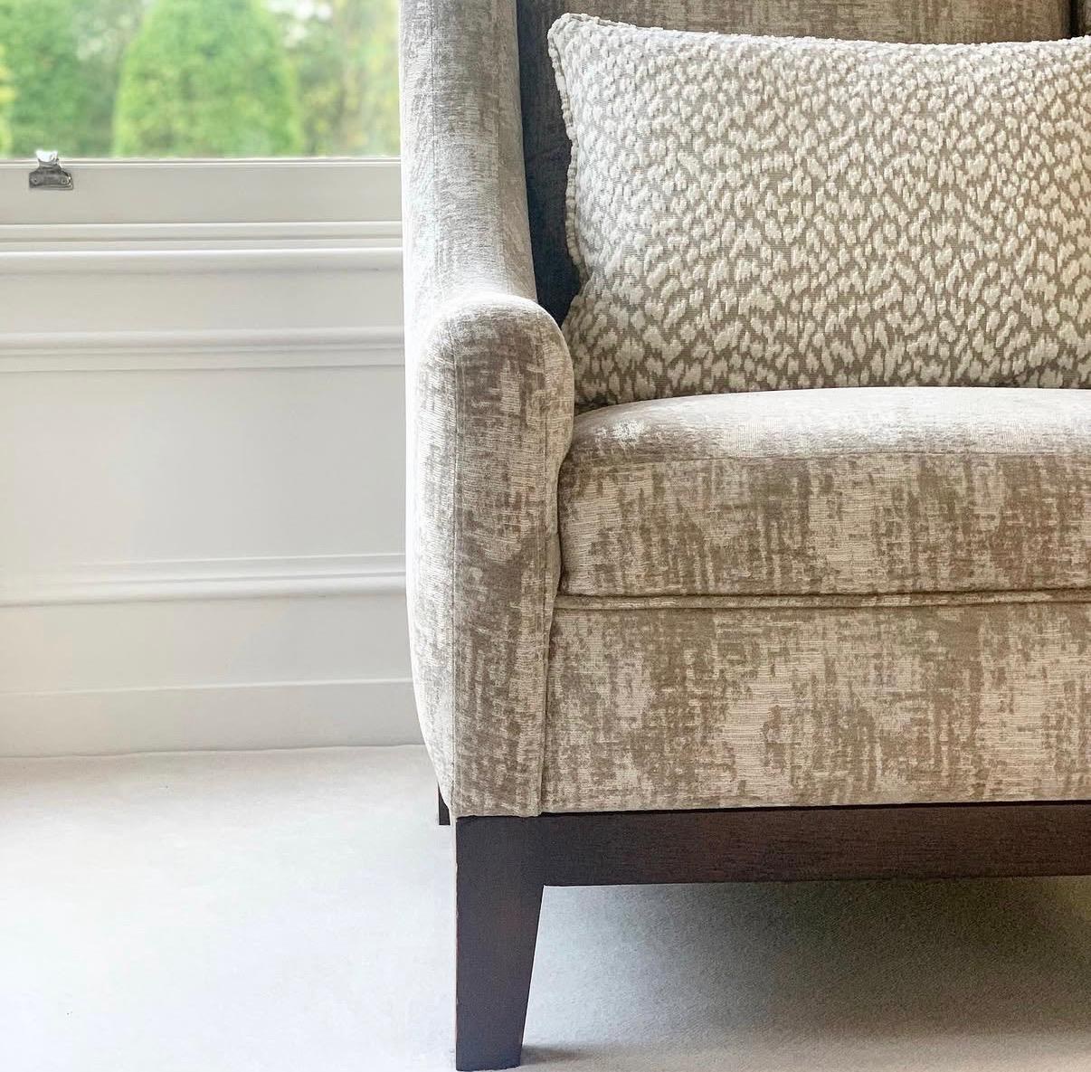 A cream textured upholstered armchair with a soft leopard-print accent cushion, in considered Casamance French fabric