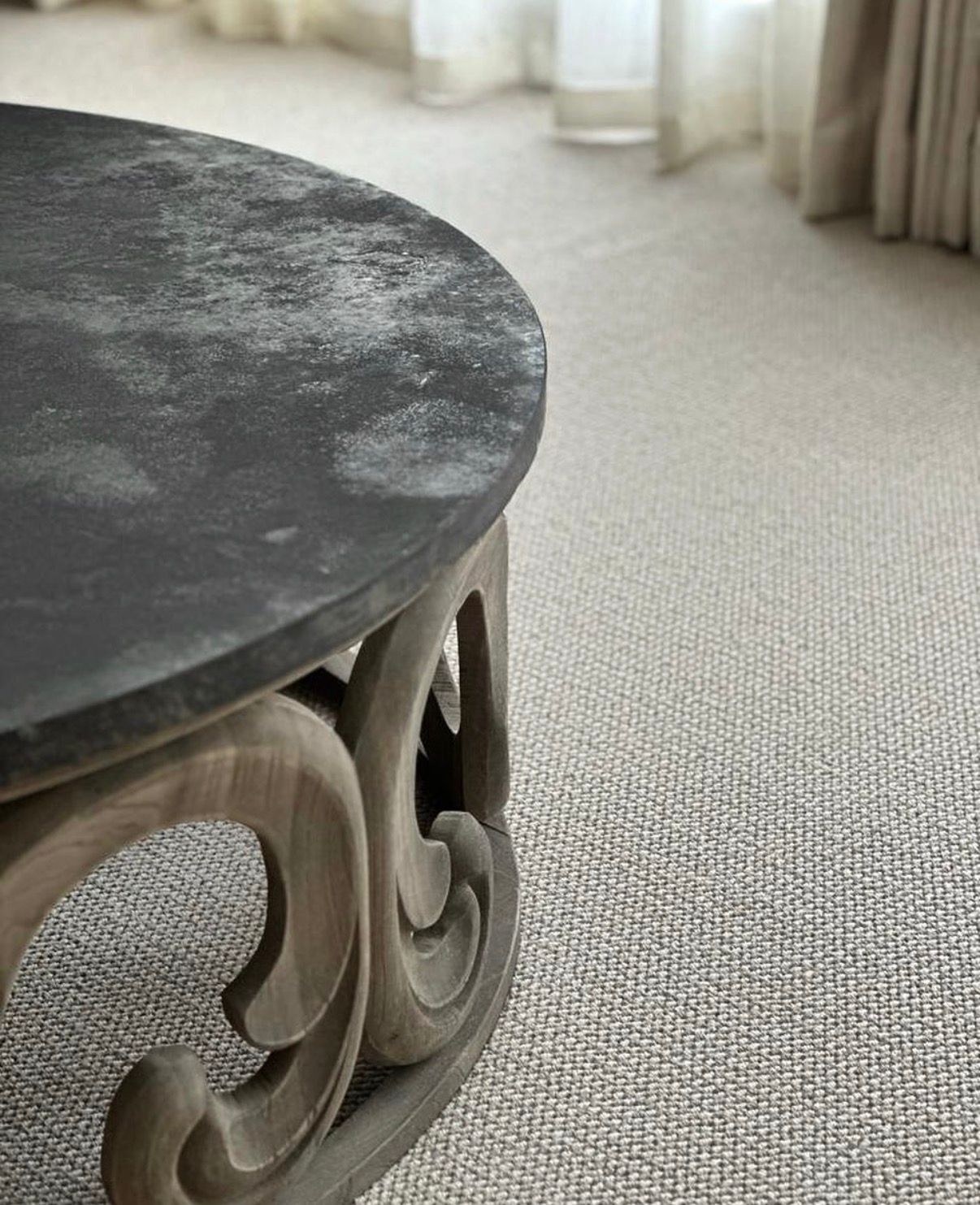 A round dark stone-topped table on a carved wooden base, sitting on a cream and oat textured natural-fibre carpet — Cavalier Carpets in a finished Aubury room
