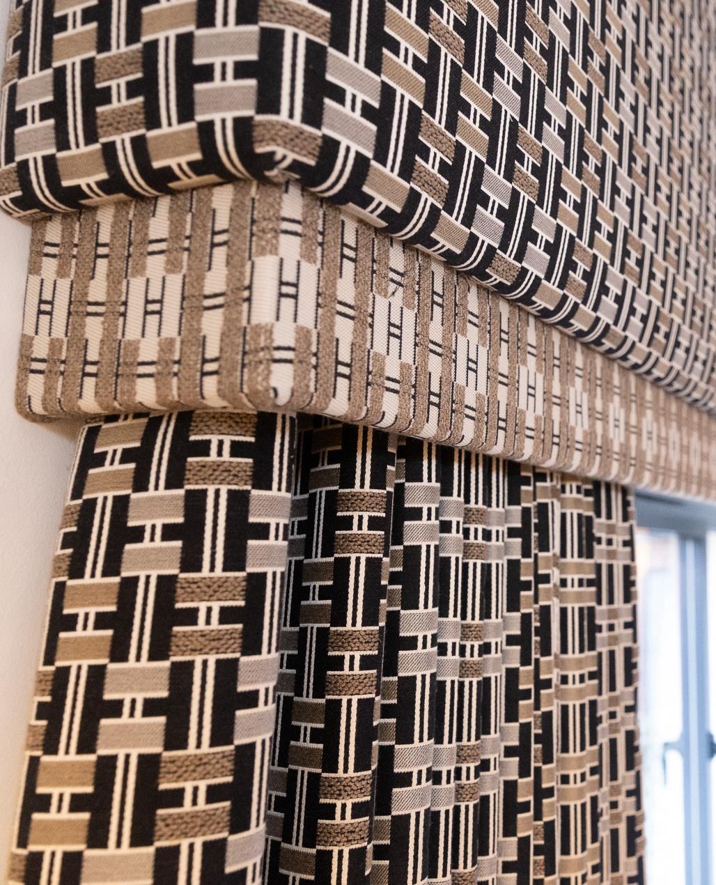 A patterned pelmet and curtain drape in black, beige and cream basket-weave, by a window — Clarke & Clarke pattern work in drapery