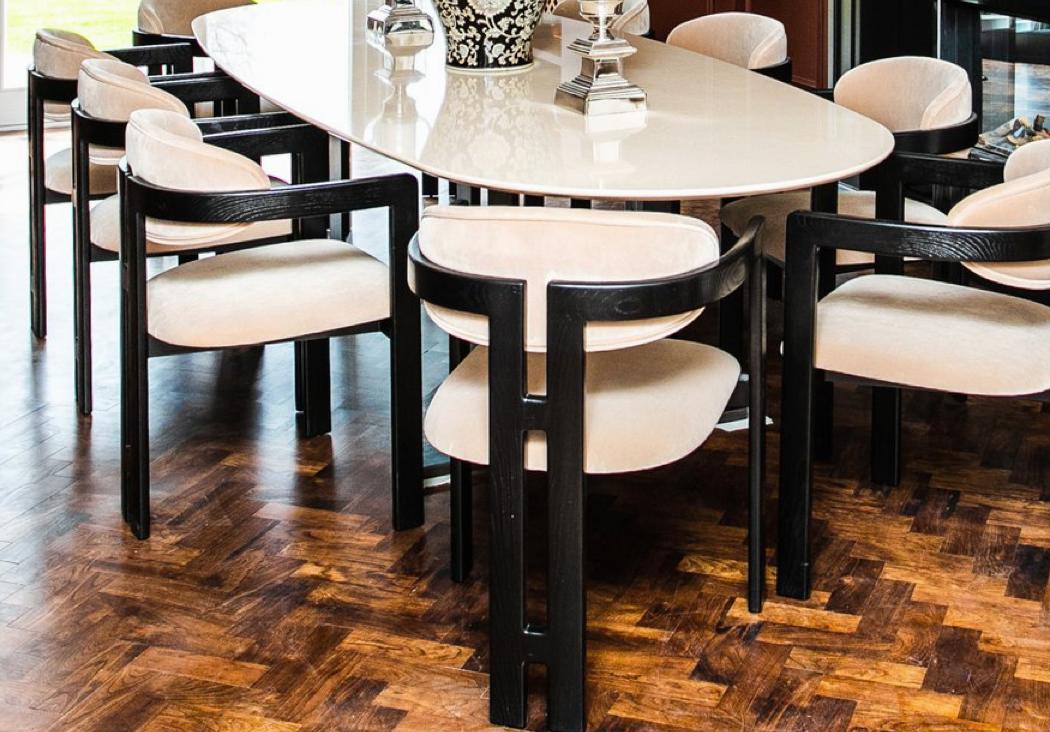 Sculptural curved-back armchairs in cream velvet on black timber frames, set around an oval cream marble dining table on dark herringbone parquet — Liang and Eimil dining furniture from a recent Aubury project