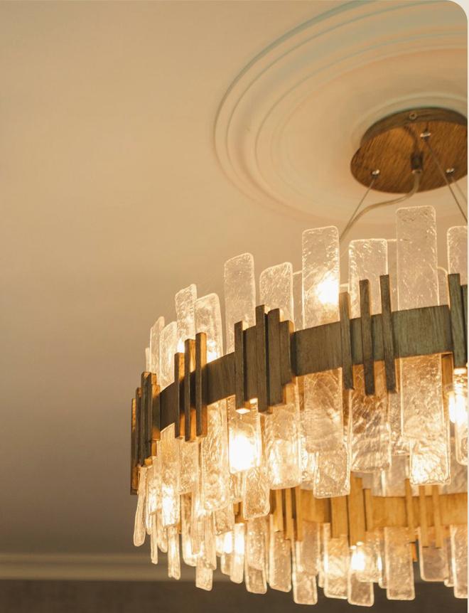 A statement chandelier with frosted glass tiles and a brass armature, hung from an ornate ceiling rose — R V Astley sculptural lighting in an Aubury project