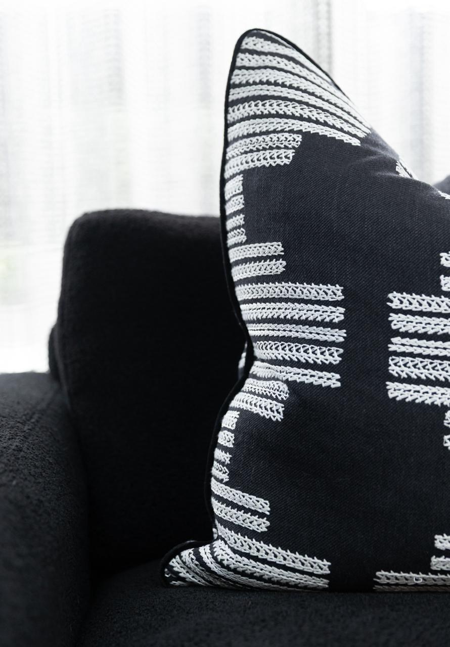 A black cushion with a white embroidered geometric motif on a black boucle sofa — a hand-loomed weave moment from Wemyss
